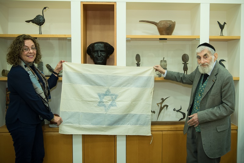 נשיאת האוניברסיטה, פרופ' רבקה כרמי והאספן עזרא גורדסקי מציגים את הדגל ההיסטורי 